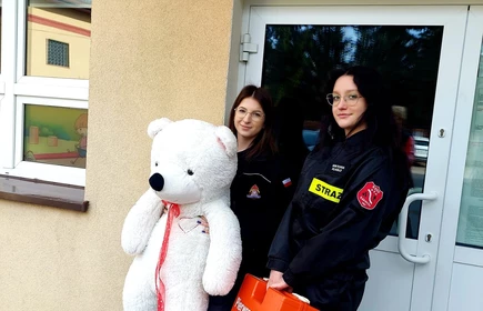 Na zdjęciu od lewej uczennice Justyna Kącka i Wiktoria Klasło wraz z misiem Heńkiem przed budynkiem Publicznego Przedszkola w Łapanowie.
