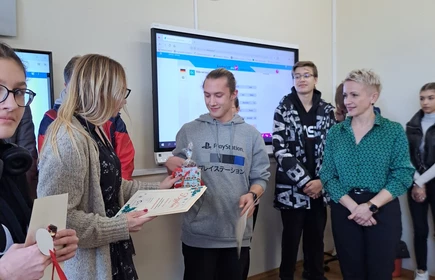 Na zdjęciu wręczenie nagród i dyplomów  uczestnikom przez panią dyrektor Dorotę Matlęgę, panią Ewę Sudziarską i panią Lucynę Zajd. Nagrodę odbiera laureat drugiego miejsca - Igor Prorok. W tle pozostali uczestnicy konkursu.