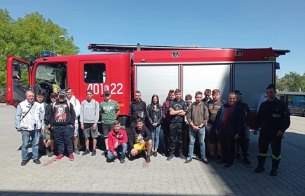 Zdjęcie grupowe młodzieży, wraz z opiekunami: Panem Wiesławem Węglarzem, Panem Józefem Kurasem oraz przedstawicielami straży. Zdjęcie na tle wozu strażackiego.  