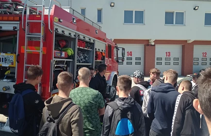 Zdjęcie młodzieży uczestniczącej w wycieczce, w tle wóz strażacki. 