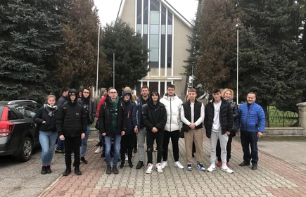 Grupowe zdjęcie uczestników wycieczki wykonane przed wyjazdem do Krakowa, na tle Kościoła pw. Redemptor Hominis w Łapanowie.