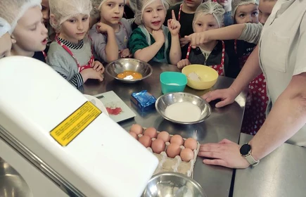 Zdjęcie przedstawia dzieci z Niepublicznego Przedszkola „Bajkowa Kraina” w Kobylcu, które uczestniczyły w warsztatach kulinarnych pieczenia babek wielkanocnych. Ponadto na fotografii Pani Małgorzata Majda-Frączek.