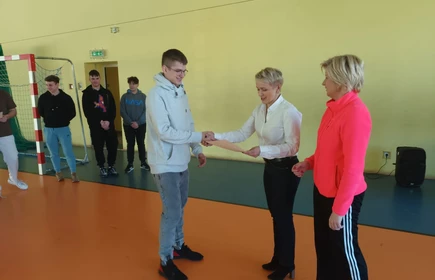 Na zdjęciu dyplom za zdobycie I miejsca w Mistrzostwach szkoły w tenisie stołowym odbiera Mikołaj Stalmach, kl. 4 AP. Dyplom wręcza pani dyrektor - mgr inż. Dorota Matlęga oraz pani Celina Jacewicz. Zdjęcie wykonane w Hali Sportowej CKZiU w Łapanowie.  