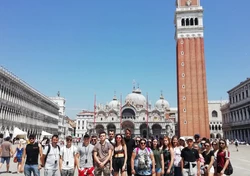 grupa ludzi pozująca do zdjęcia przed wysoką wieżą z Piazza San Marco w tle