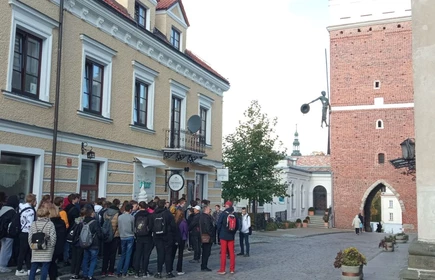 Młodzież na tle Bramy Opatowskiej, w tle widoczna figura flisaka balansującego na linie