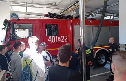 Zdjęcie młodzieży uczestniczącej w wycieczce, w tle wóz strażacki. 