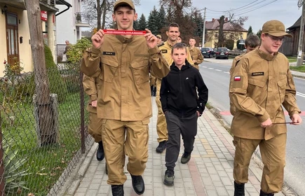 Na zdjęciu uczniowie klasy pożarniczej CKZiU w Łapanowie wraz mieszkańcami Łapanowa i okolic podczas akcji „Noś odblaski”. Fotografia barwna wykonana w centrum Łapanowa.