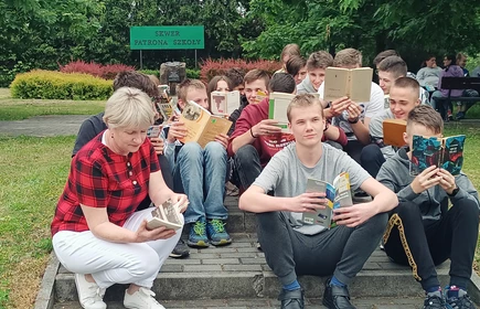 Fotografia barwna: klasa I SB wraz z wychowawcą panią Maria Plewą podczas akcji „Jak nie czytam, jak czytam". Zdjęcie wykonano na Skwerze Patrona Szkoły.