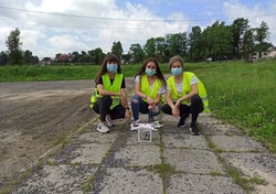 Trzy uczestniczki kursu w żółtych kamizelkach odblaskowych, kucające przy dronie.