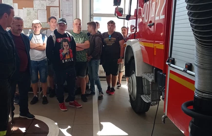 Po lewej stronie młodzież uczestnicząca w wycieczce, po prawej wóz strażacki. 
