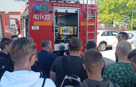 Zdjęcie młodzieży uczestniczącej w wycieczce, w tle wóz strażacki. 