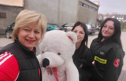 Na zdjęciu od lewej pani Celina Jacewicz oraz uczennice: Justyna Kącka i Wiktoria Klasło wraz z misiem Heńkiem przed Halą Sportową CKZiU w Łapanowie.